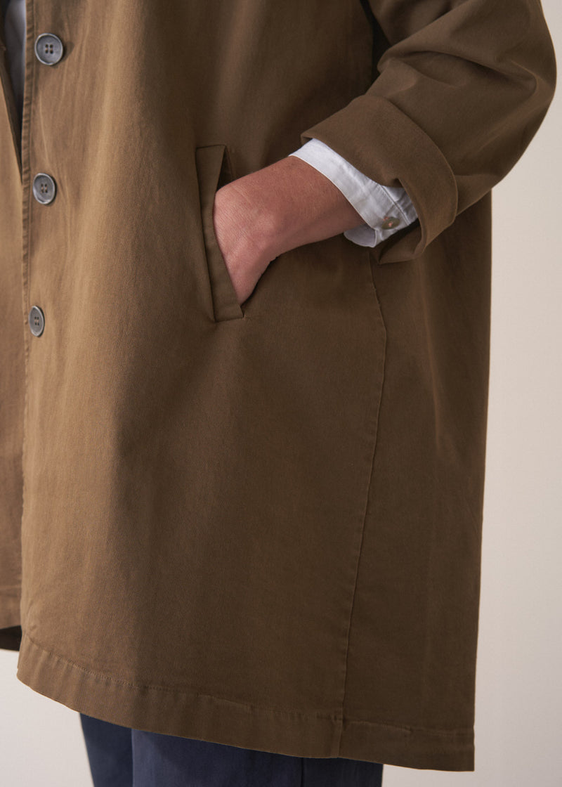 Woman wearing a khaki brown short trench coat over a white shirt on a plain background