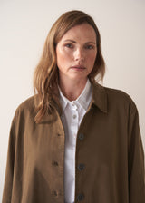 Woman wearing a khaki brown short trench coat over a white shirt on a plain background
