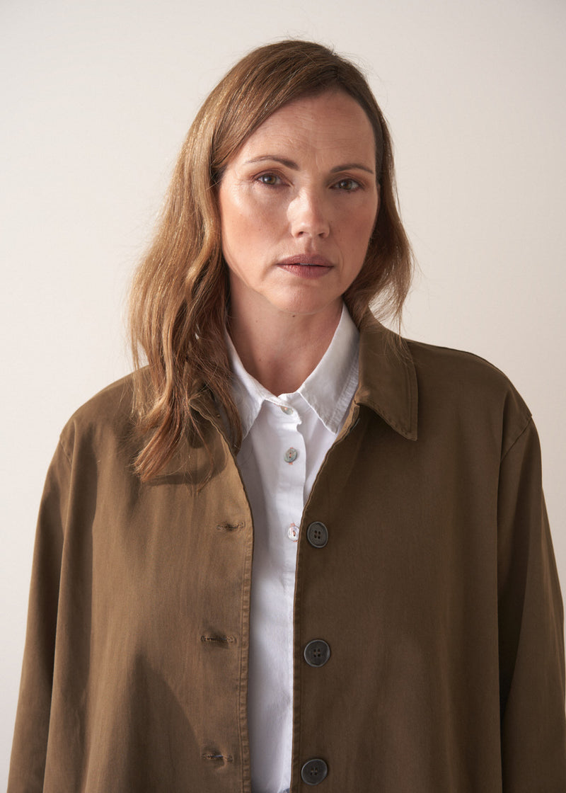 Woman wearing a khaki brown short trench coat over a white shirt on a plain background