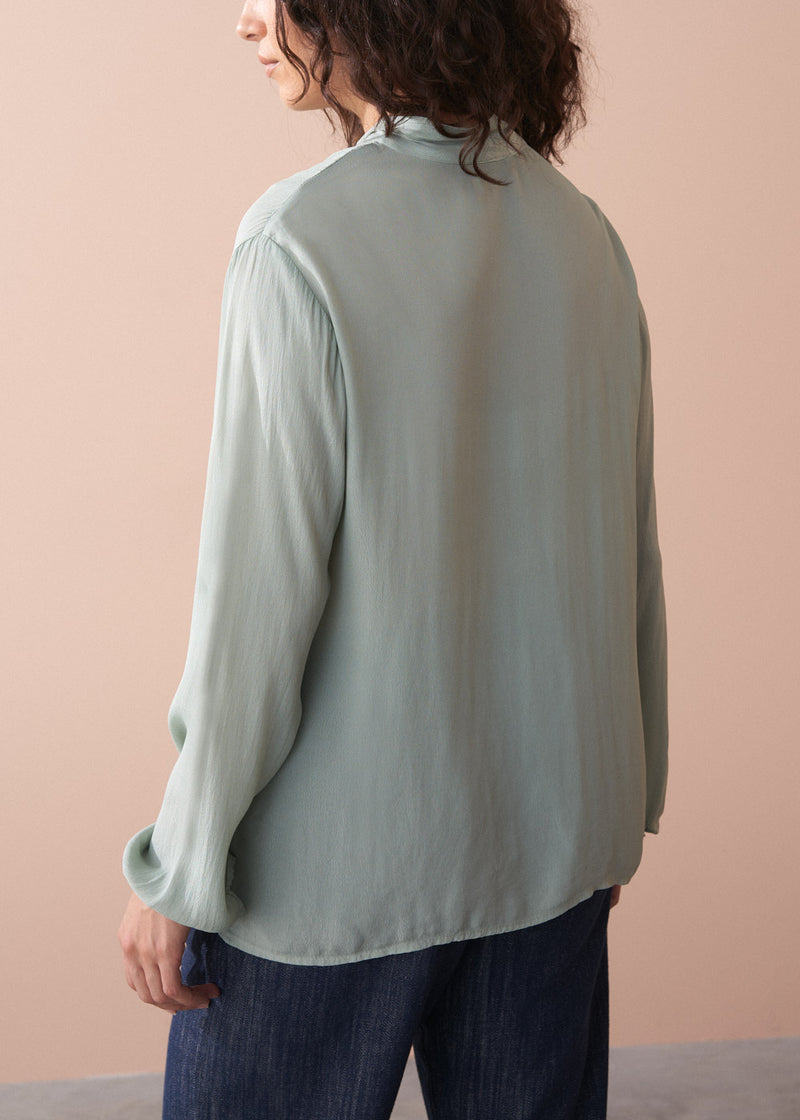 Person wearing a light green blouse against a pink background