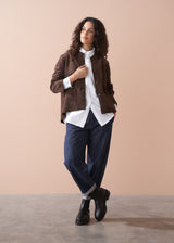 Woman wearing a brown faux suede jacket over a white shirt with a beige background
