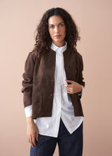 Woman wearing a brown faux suede jacket over a white shirt with a beige background