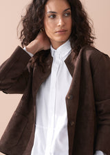Woman wearing a brown faux suede jacket over a white shirt with a beige background