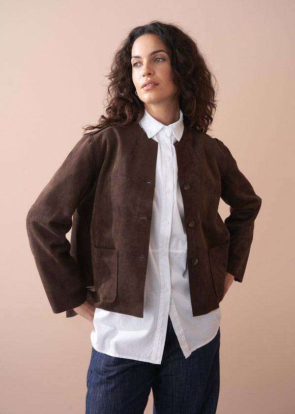 Woman wearing a brown faux suede jacket over a white shirt with a beige background