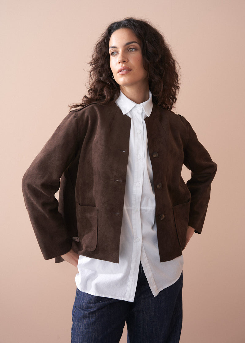 Woman wearing a brown faux suede jacket over a white shirt with a beige background
