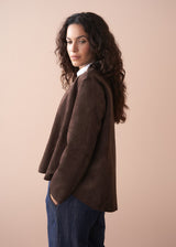 Woman wearing a brown faux suede jacket over a white shirt with a beige background