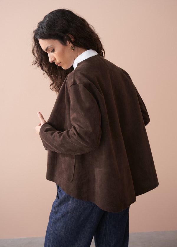 Woman wearing a brown faux suede jacket over a white shirt with a beige background