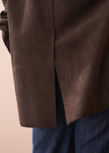 Woman wearing a brown faux suede jacket over a white shirt with a beige background