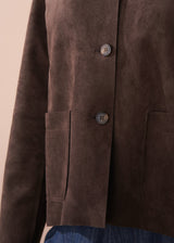 Woman wearing a brown faux suede jacket over a white shirt with a beige background