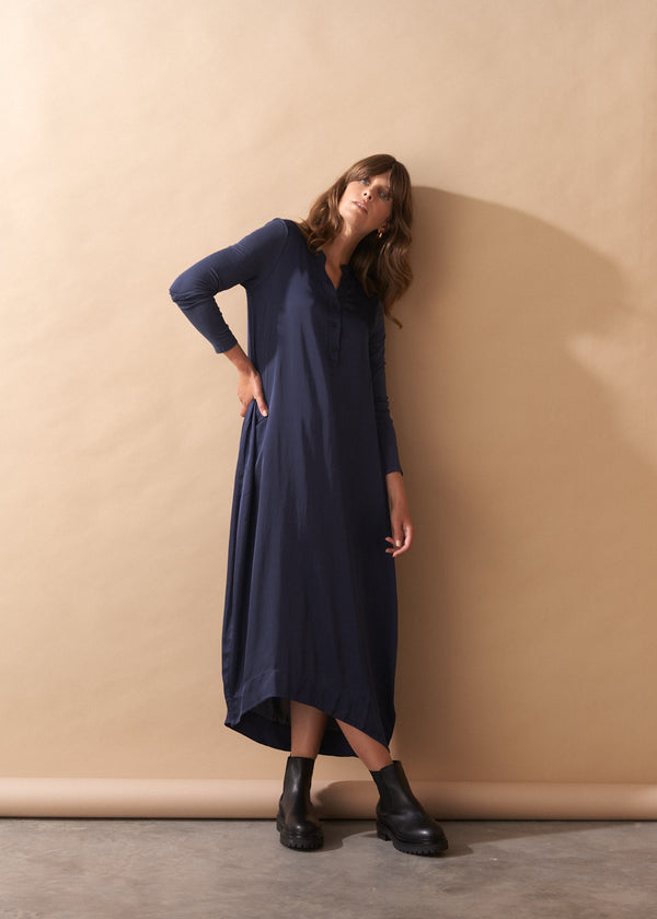 Woman wearing a long navy dress against a beige wall