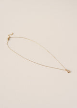 A delicate gold chain necklace with a small heart-shaped pendant, displayed on a textured off-white background.