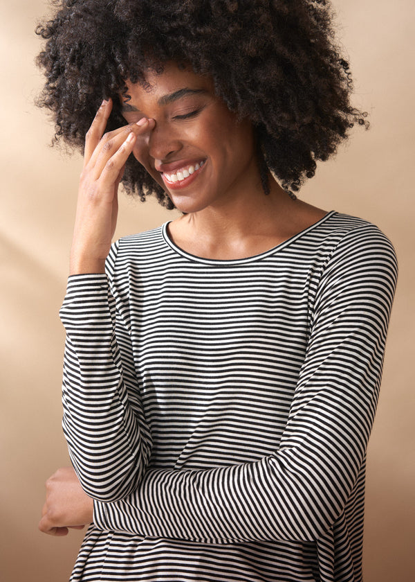 Woman wearing a black and white striped long-sleeve top against a beige background