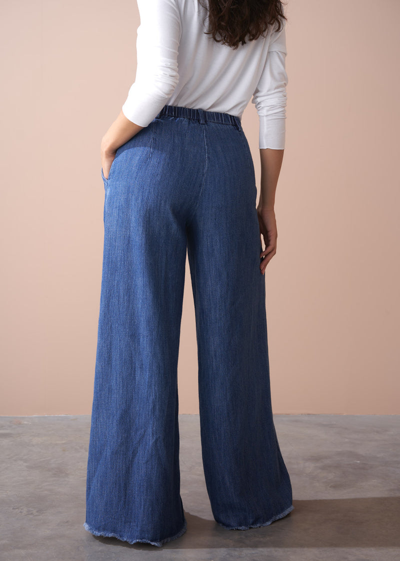 Person wearing blue wide-leg jeans against a beige background