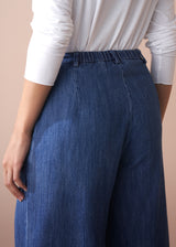 Person wearing blue denim pants with a white long-sleeve shirt on a beige background