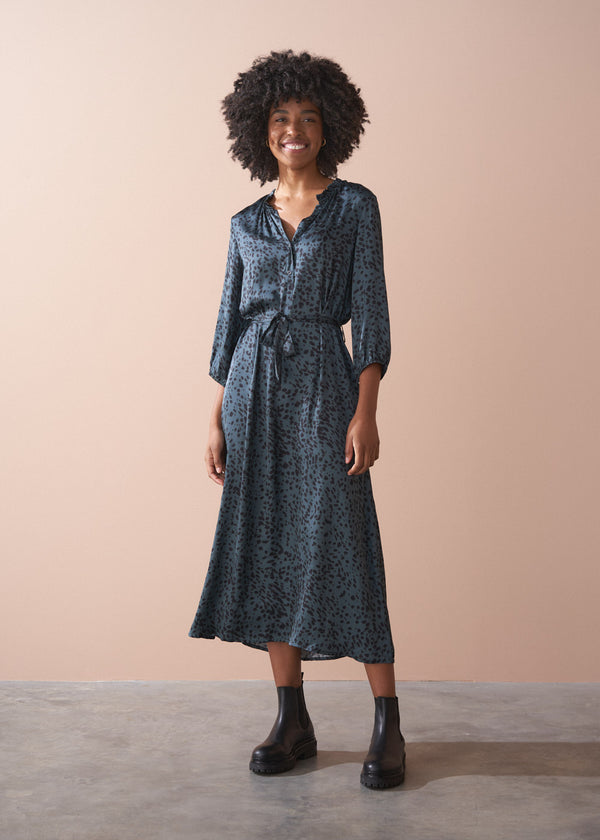 Woman wearing a blue patterned dress with black boots against a beige background