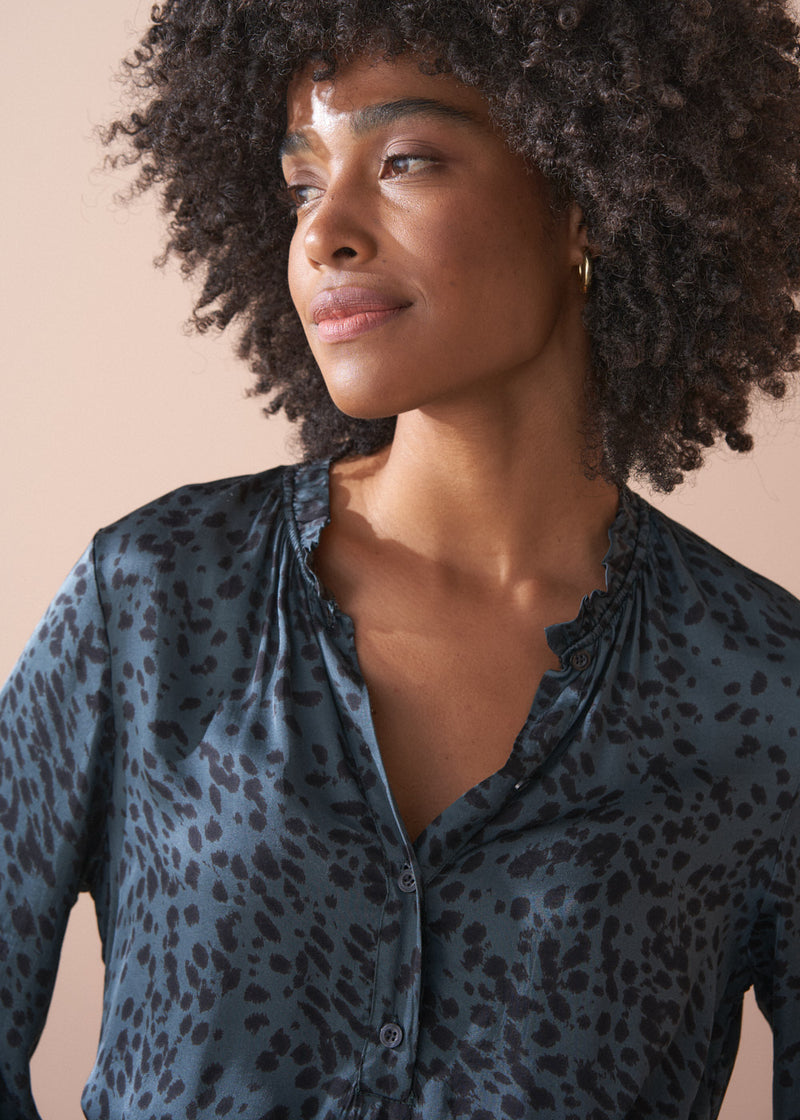 Woman wearing a dark blue satin shirt with a leopard print pattern against a beige background
