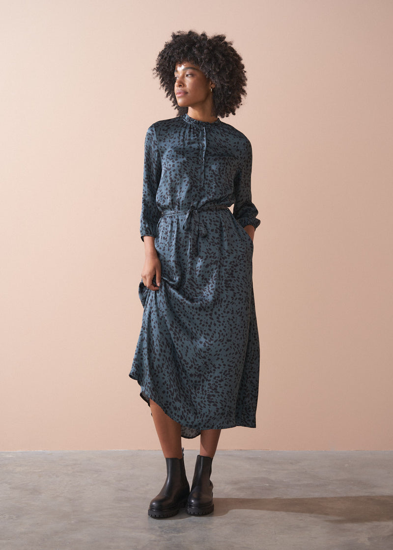Woman wearing a patterned dress standing against a beige wall.