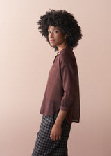 Person wearing a brown semi sheer shirt and plaid pants against a beige background