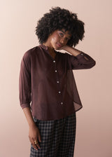 Woman wearing a semi sheer brown blouse with rolled-up sleeves against a beige background