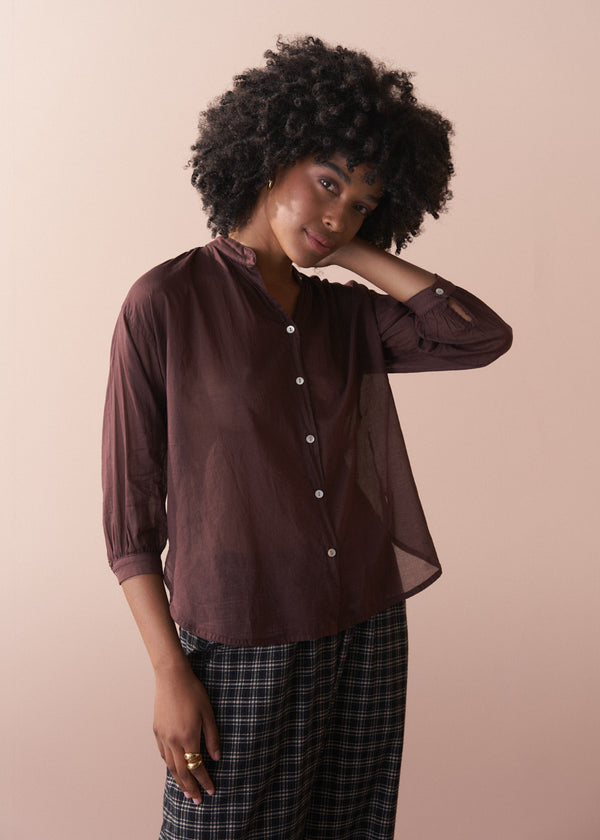 Woman wearing a semi sheer brown blouse with rolled-up sleeves against a beige background