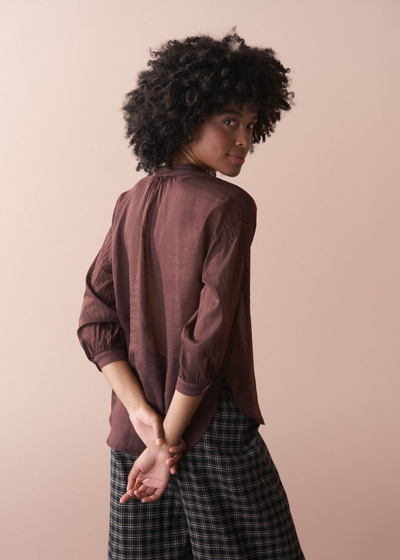 Woman wearing a brown shirt and plaid pants against a beige background