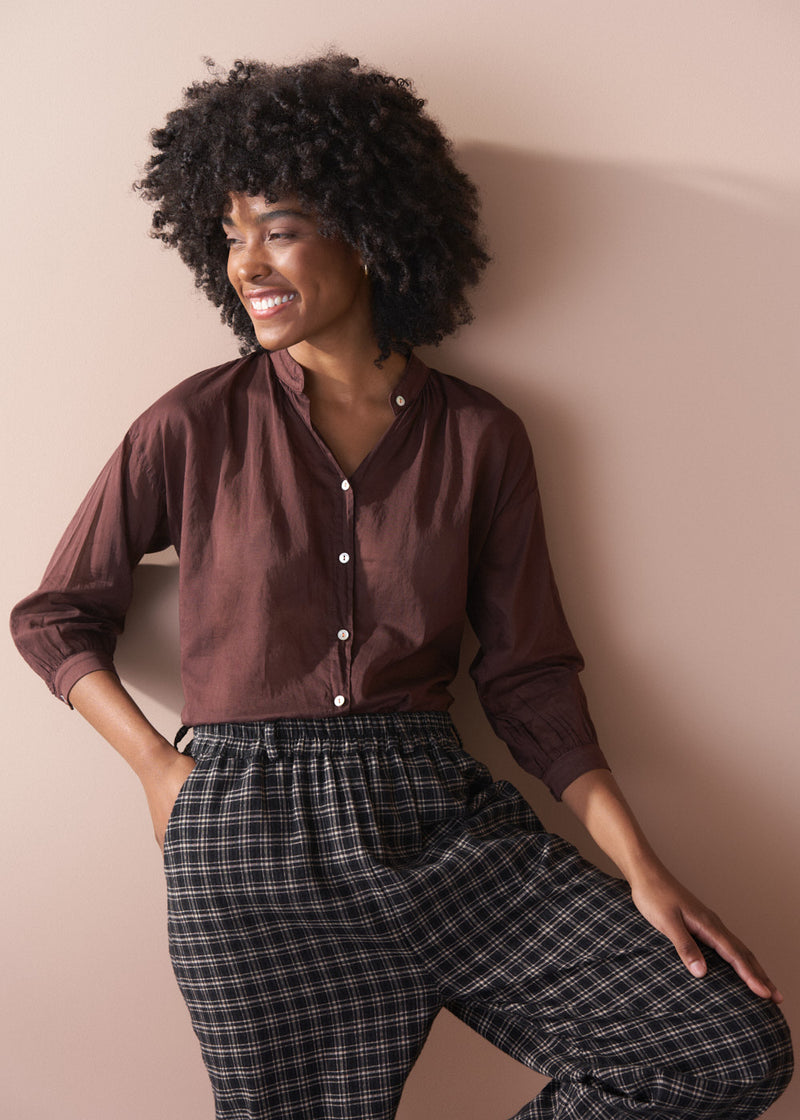 Woman wearing a brown shirt and plaid pants against a beige wall