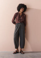 Person wearing a brown shirt and plaid pants against a beige wall.