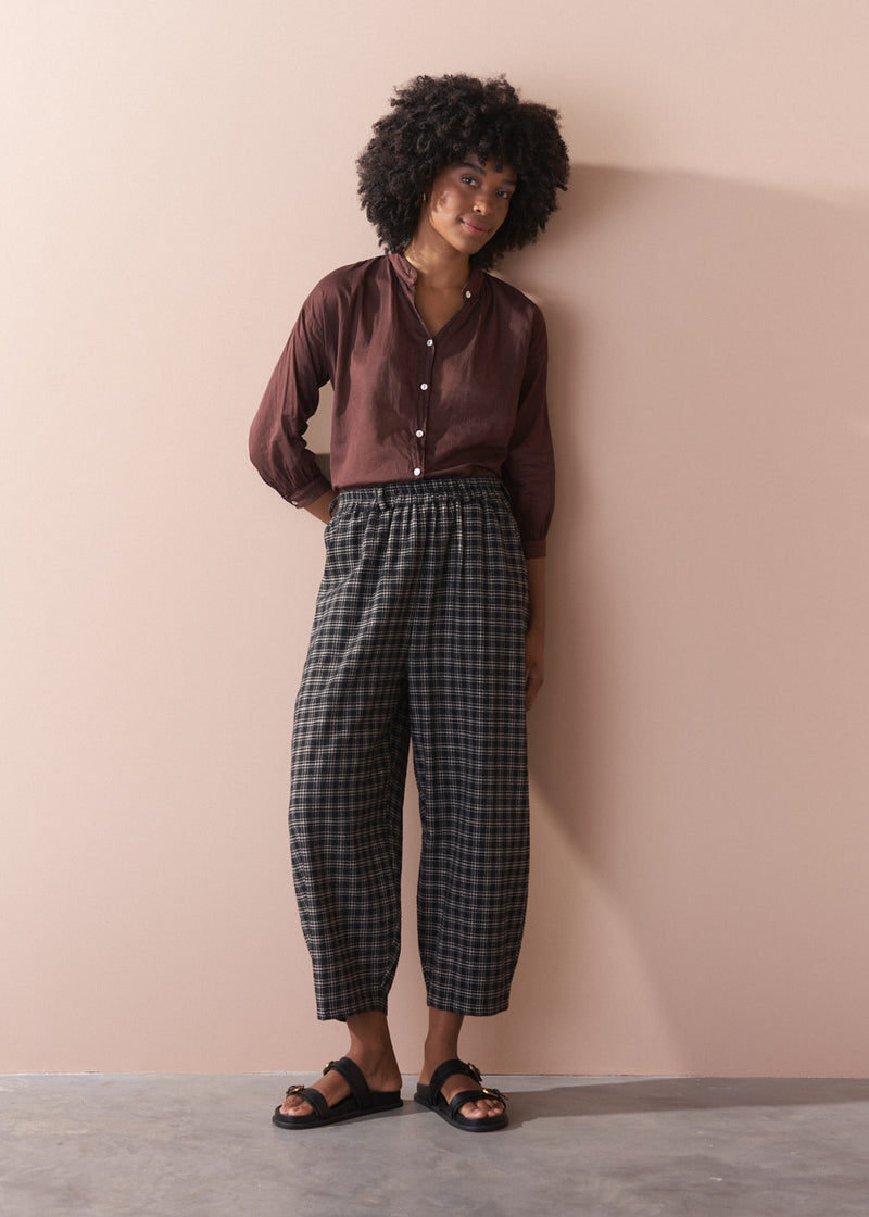 Person wearing a brown shirt and plaid pants against a beige wall.