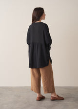 Woman wearing a black cotton oversized blouse and brown linen trousers
