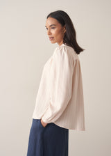 Woman wearing a light pink blouse with pinstripes and long sleeves with dark navy trousers