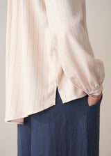 Woman wearing a light pink blouse with pinstripes and long sleeves with dark navy trousers