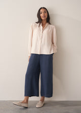 Woman wearing a light pink blouse with pinstripes and long sleeves with dark navy trousers