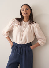 Woman wearing a light pink blouse with pinstripes and long sleeves with dark navy trousers