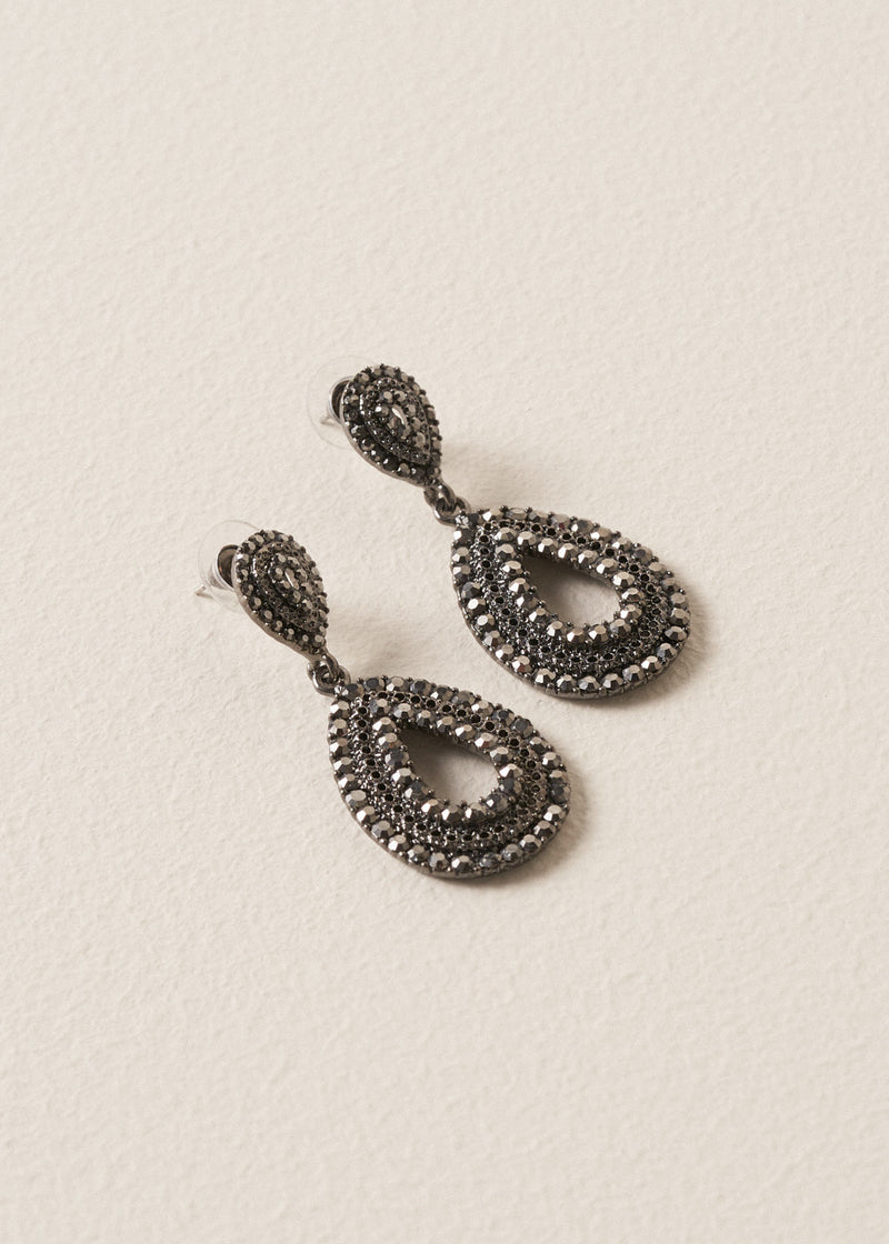 A pair of Ainsley Earrings featuring a striking teardrop silhouette embellished with jet-black crystals, on a beige background