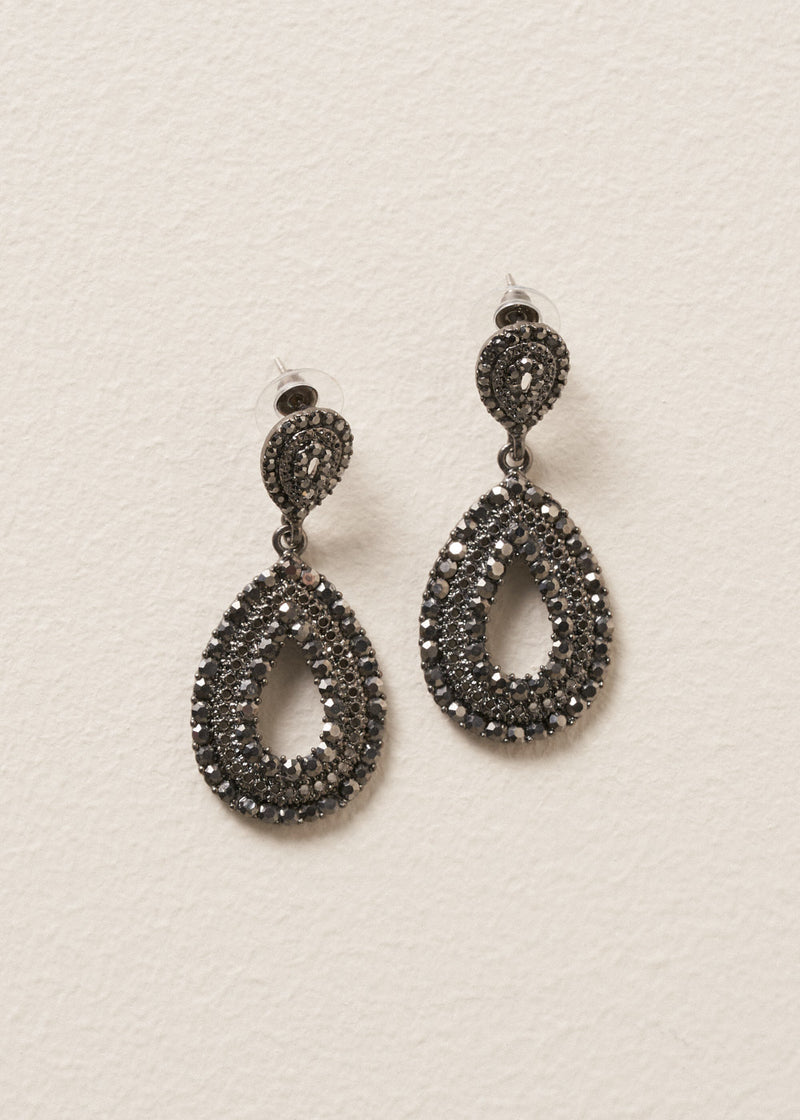 A pair of Ainsley Earrings featuring a striking teardrop silhouette embellished with jet-black crystals, on a beige background