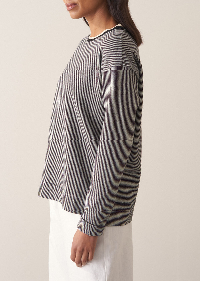 Woman wearing a grey stripe sweater and white jeans against a plain background