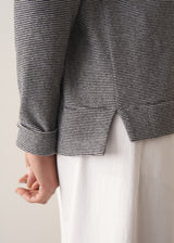 Woman wearing a grey stripe sweater and white jeans against a plain background