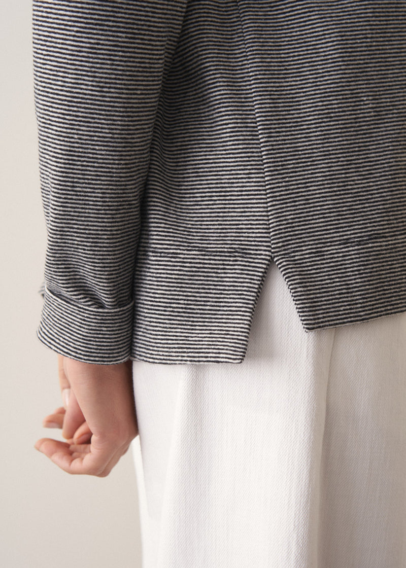 Woman wearing a grey stripe sweater and white jeans against a plain background