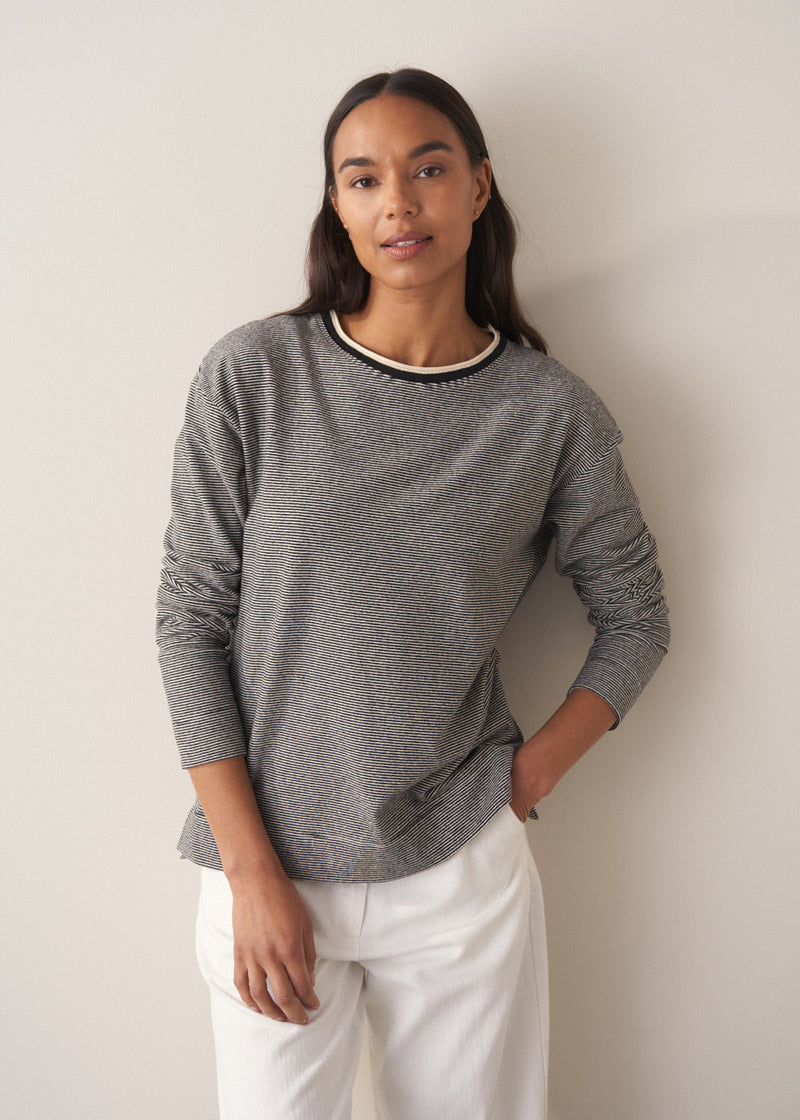 Woman wearing a grey stripe sweater and white jeans against a plain background