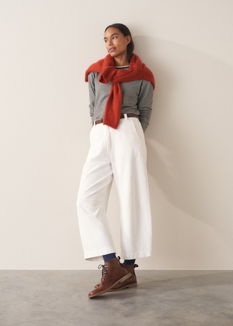 Woman wearing a grey stripe sweater and white jeans against a plain background