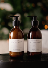 Amber glass bottle of hand lotion with pump and 'Alchemist' label on a beige background