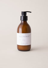 Amber glass bottle of hand lotion with pump and 'Alchemist' label on a beige background