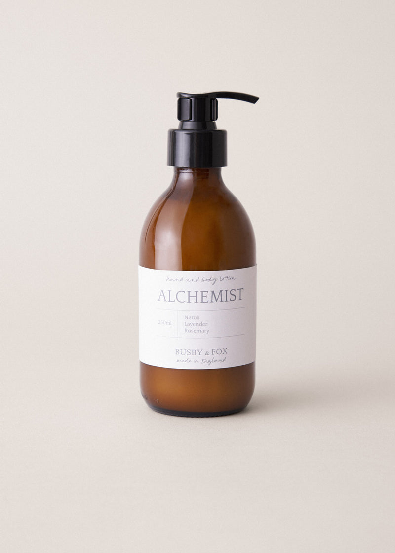 Amber glass bottle of hand lotion with pump and 'Alchemist' label on a beige background