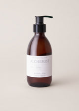 Hand and body wash in an amber bottle with black pump and "Alchemist" branding, on a beige background