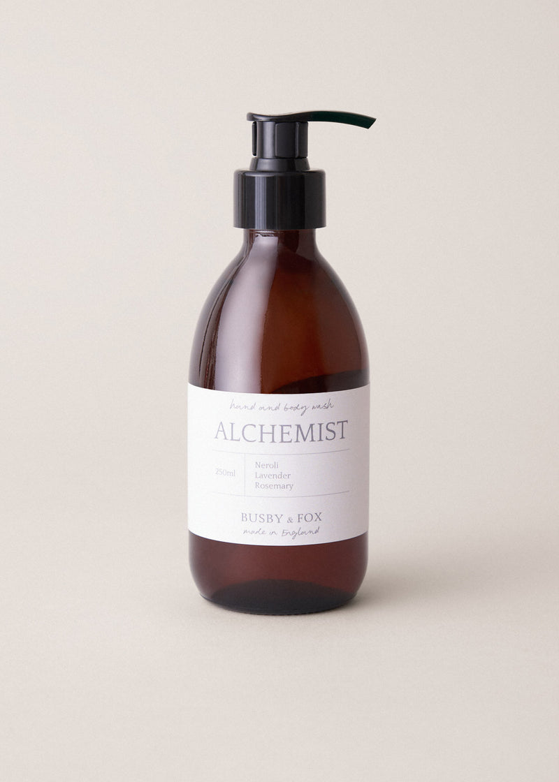 Hand and body wash in an amber bottle with black pump and "Alchemist" branding, on a beige background