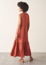 Woman wearing dark orange satin tiered floaty summer dress against a plain background