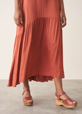 Woman wearing dark orange satin tiered floaty summer dress against a plain background