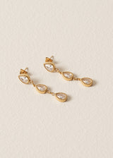 Three tier gold earrings with clear crystals on a beige background