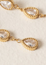 Close up of crystals on three tier gold earrings, on beige background
