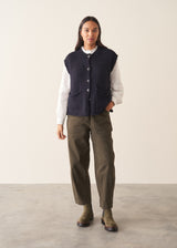 Woman wearing a dark navy blue sleeveless chunky knit waistcoat with green trousers and a white shirt
